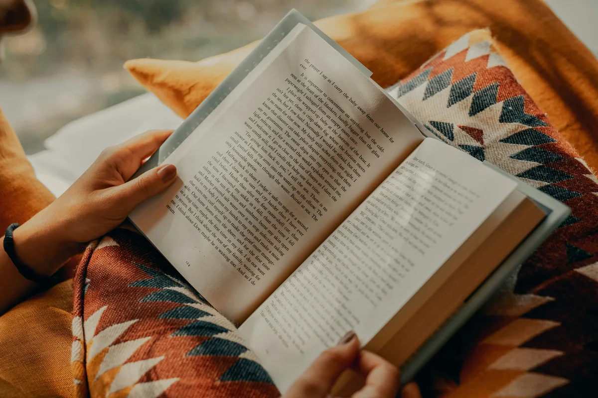 Person reading a book under a cozy blanket, representing mental-health guides